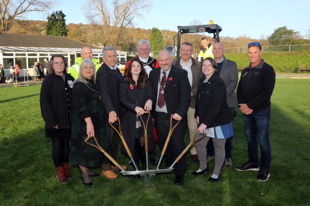Photo of a group of people gathered around a spade, ready to dig into turf.